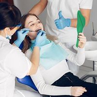 Dentist cleaning a patient’s teeth while an assistant holds tools in a bright clinic