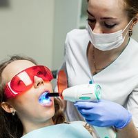 Dentist using a blue curing light on a patient wearing red protective glasses and a mask