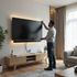 Man adjusts the top edge of a large TV mounted on a wall with glowing lights.