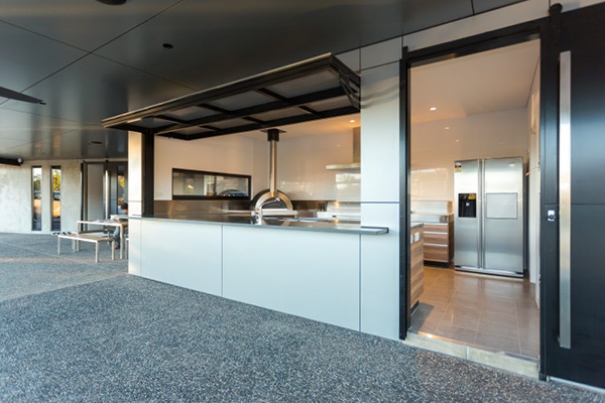 An outdoor kitchen with stainless steel appliances, a black canopy, and a concrete patio.