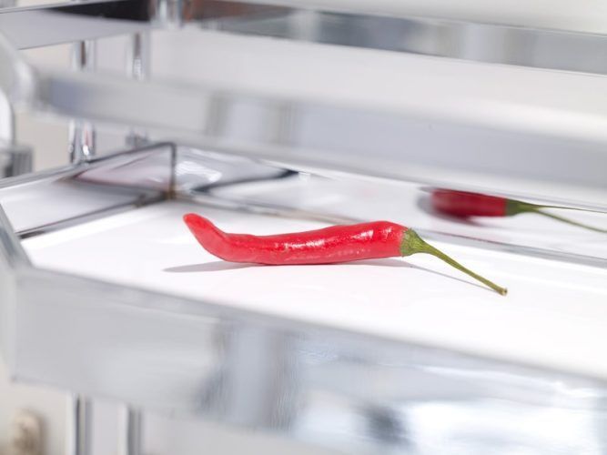 Red chili pepper on a white shelf, with a mirrored reflection.