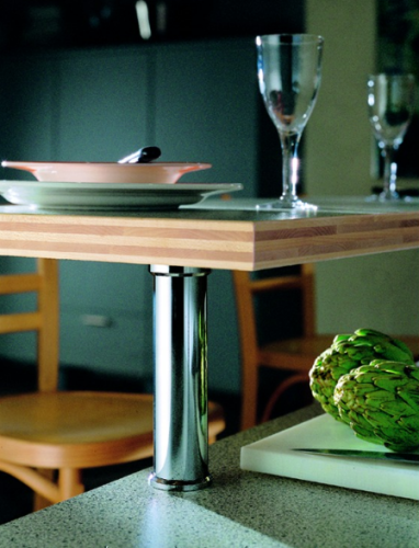 Wooden counter with a chrome leg, set with plates, glasses, and artichokes.
