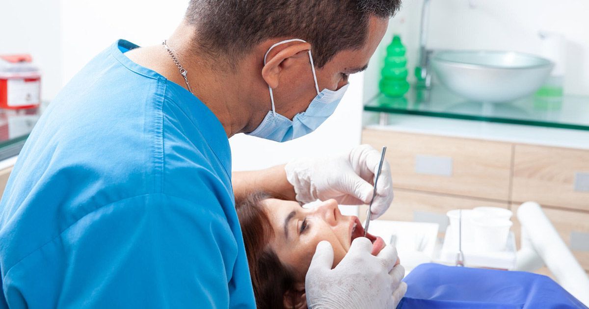 A dentist is examining a woman 's teeth in a dental office.