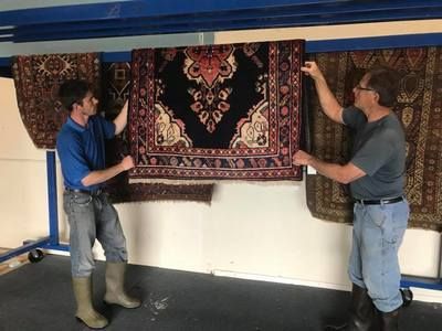 Two men are holding a rug in their hands in a room.