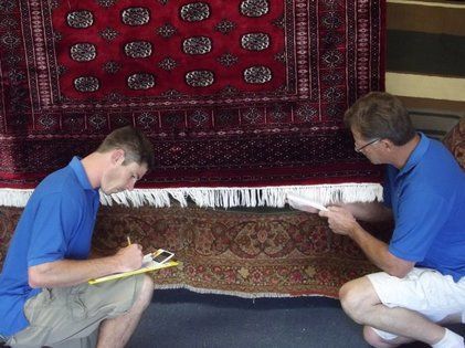 Two men in blue shirts are working on a rug