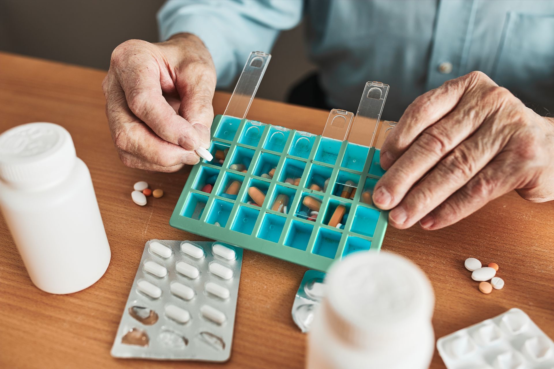 An elderly man is taking a pill out of a pill box.