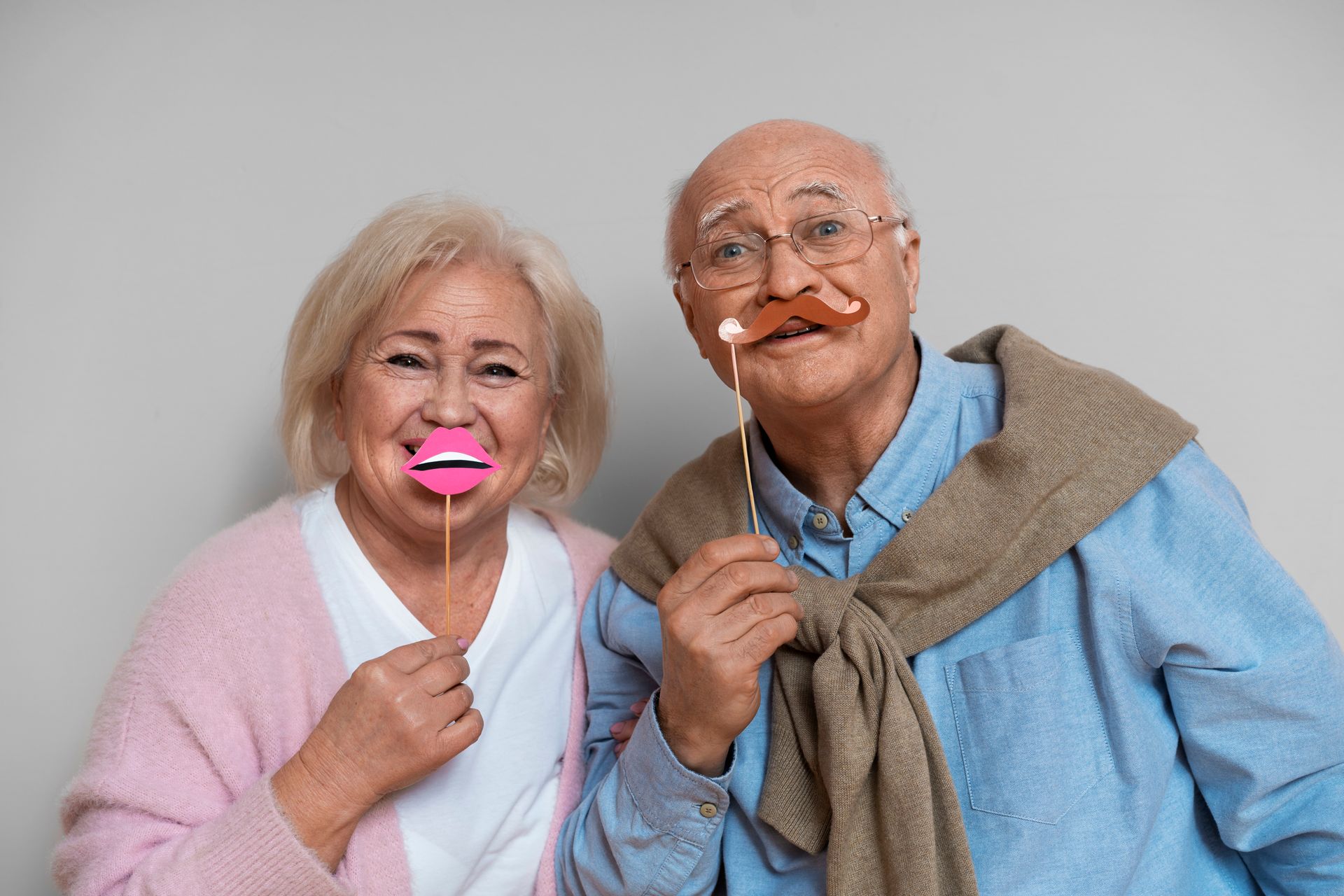 A man and a woman are holding fake mustaches in their mouths.