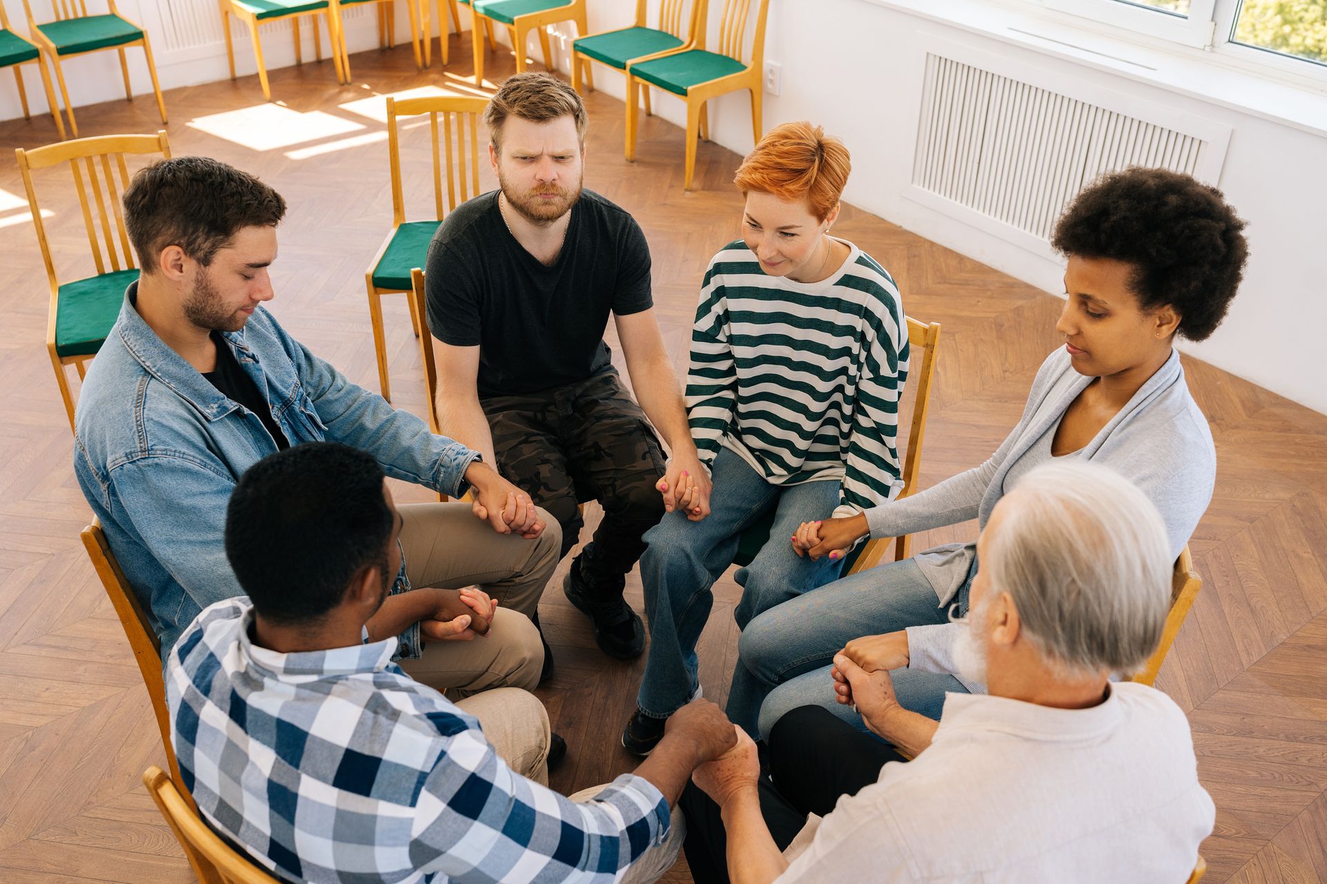 A group of people are sitting in a circle holding hands.