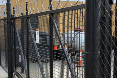 A fence with barbed wire on it is surrounding a building. A fence with barbed wire on it is surrounding a building.