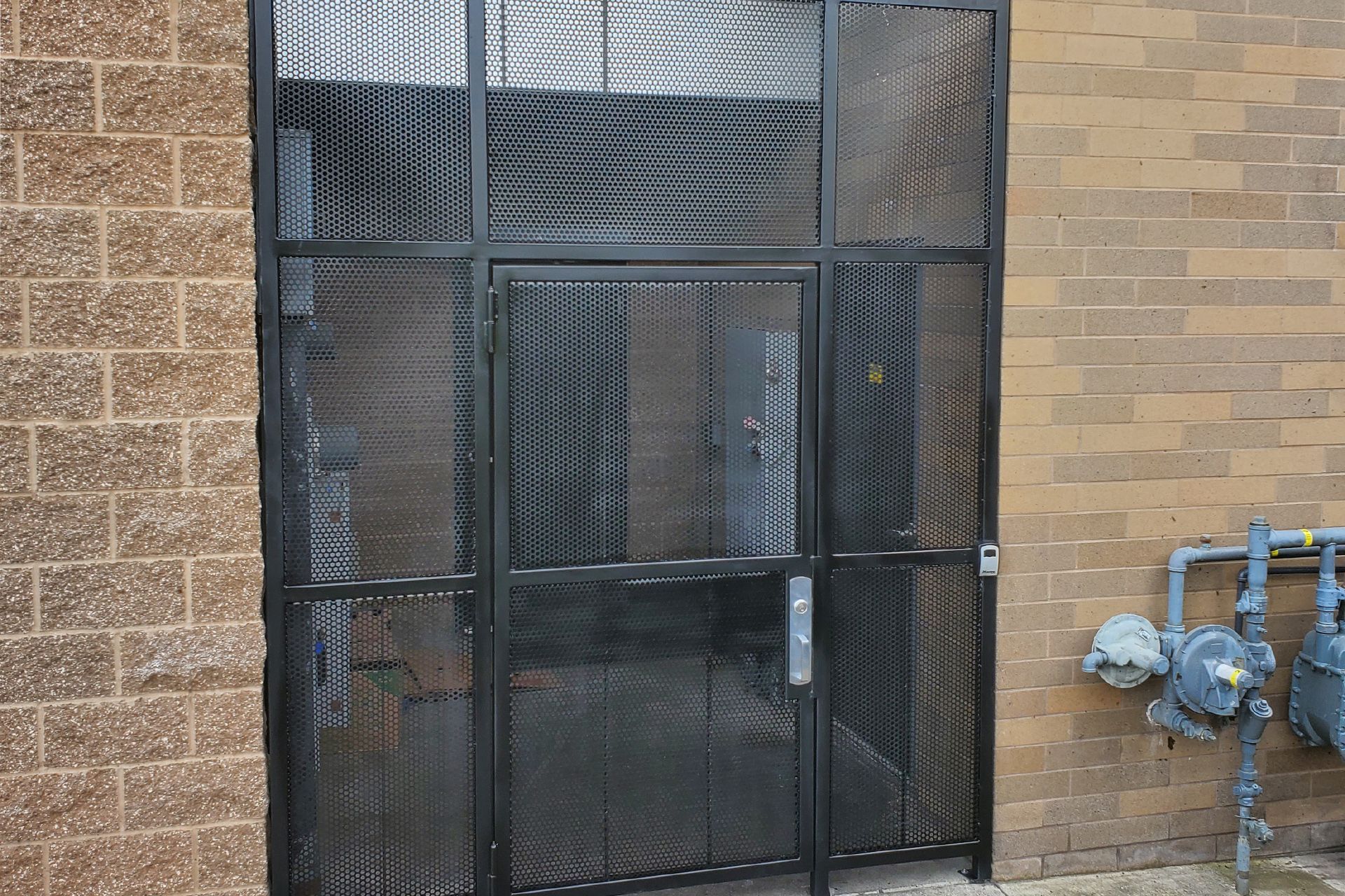 A metal gate is sitting on the side of a brick building. A metal gate is sitting on the side of a brick building.