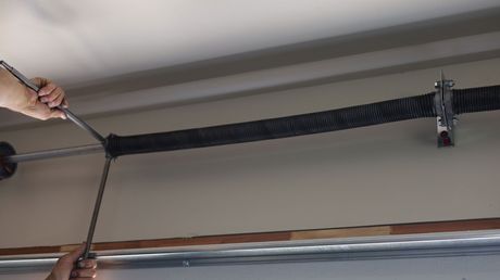 Person using a winding bar to adjust a garage door spring, mounted on the ceiling. Person using a winding bar to adjust a garage door spring, mounted on the ceiling.