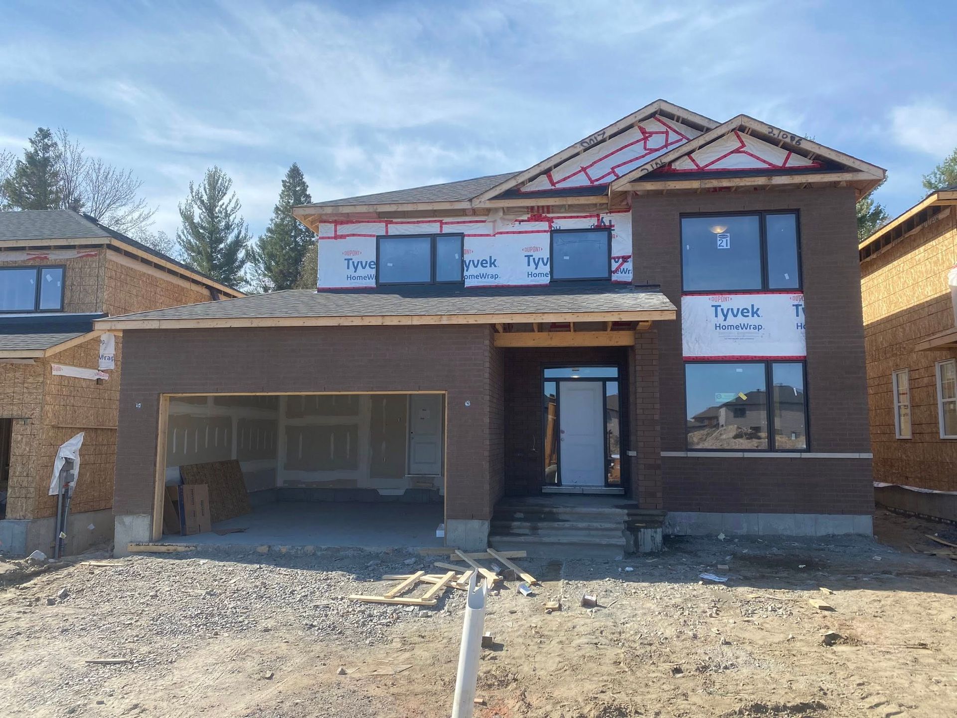 Maison à deux étages en construction avec revêtement brun et grandes fenêtres.