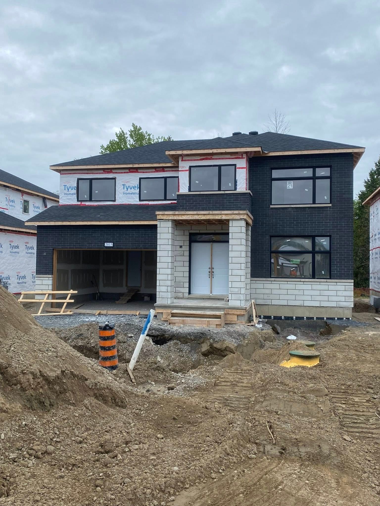 Maison neuve en construction, revêtement extérieur noir, façade non finie, garage, ciel nuageux.