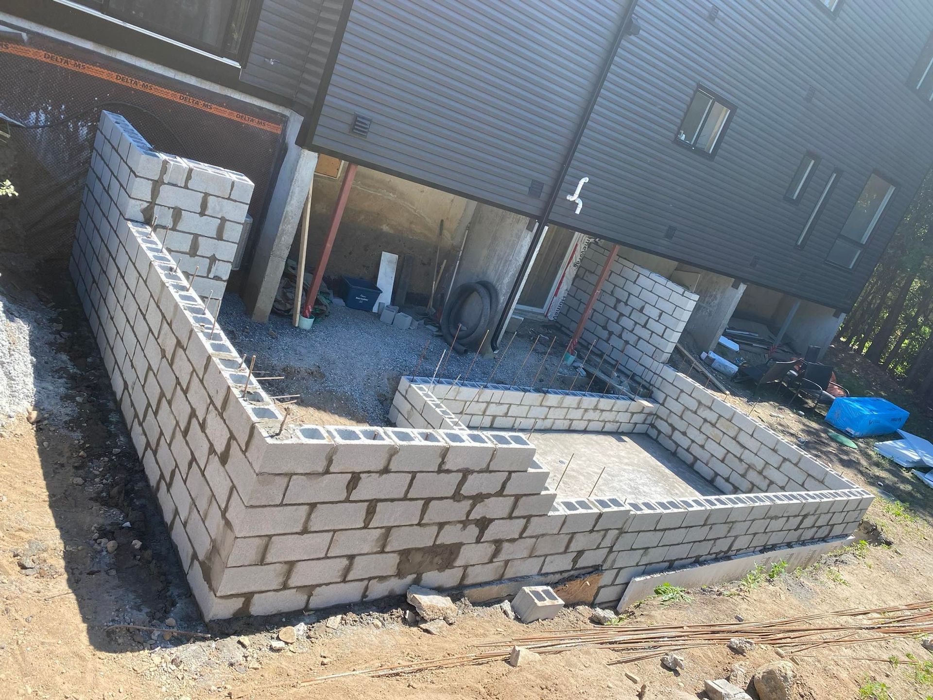 Chantier de construction avec murs en parpaings devant un bâtiment gris foncé.