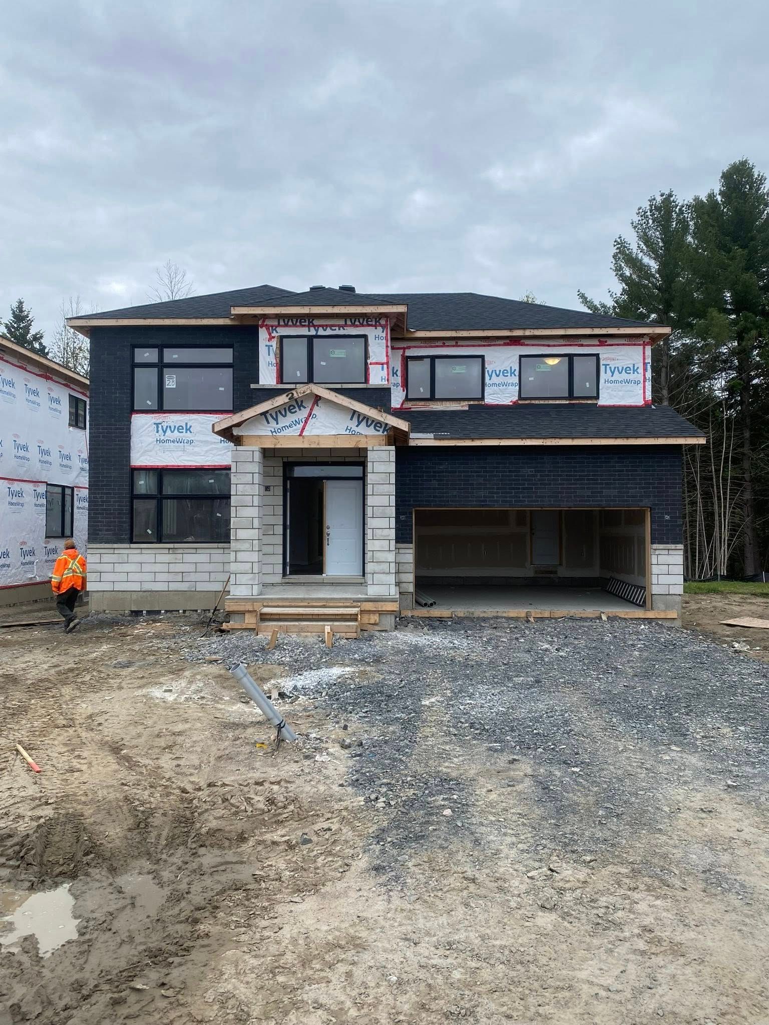 Maison en construction, extérieur noir, deux étages, avec garage ouvert, ciel nuageux.