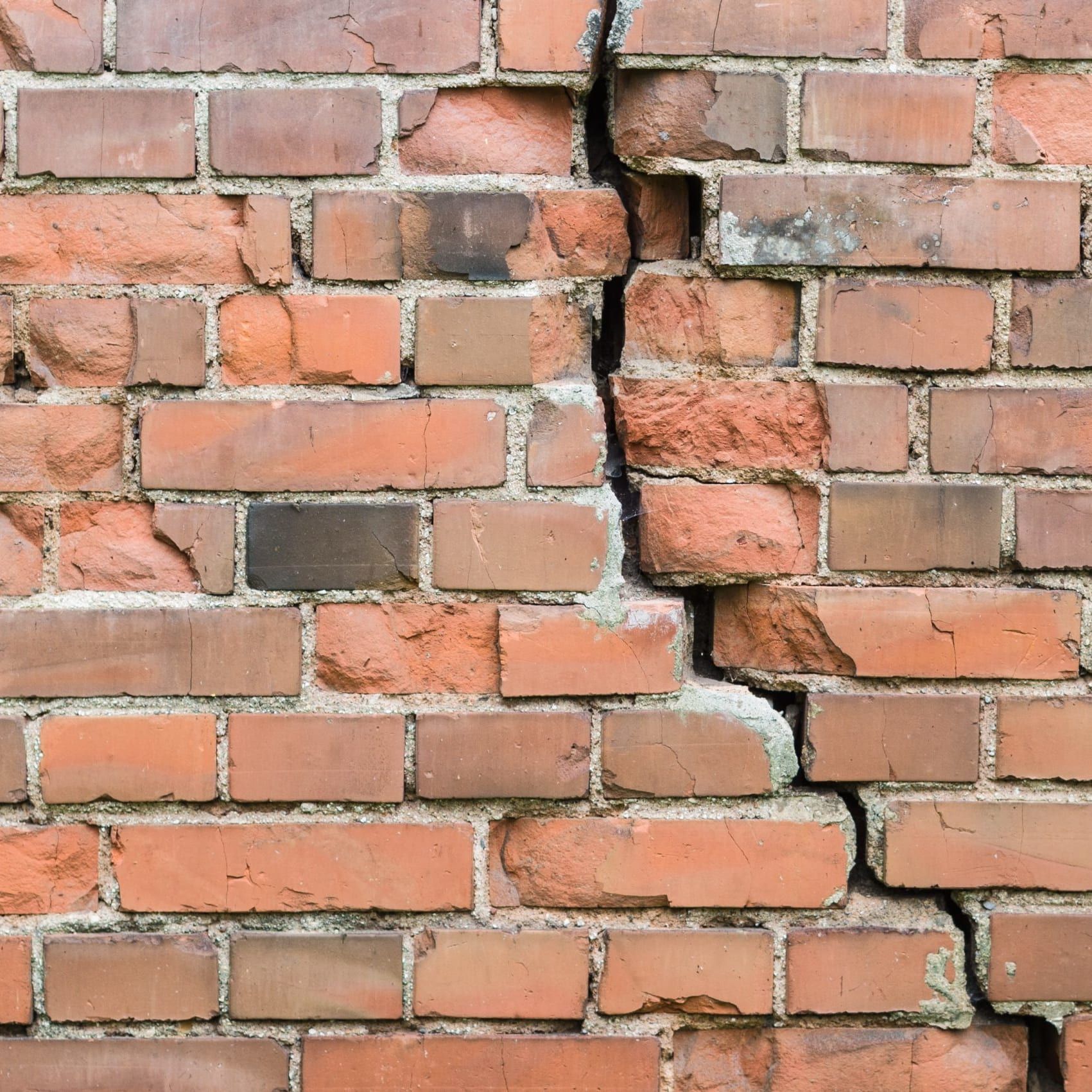 Mur de briques fissuré avec une fissure verticale, briques oranges.