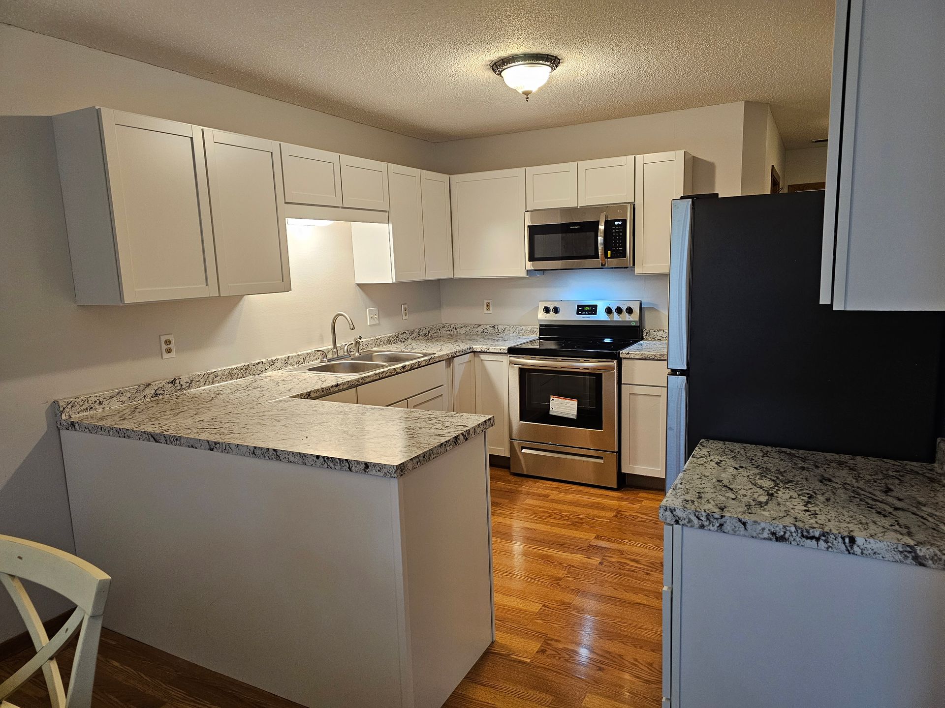 A kitchen with white cabinets , stainless steel appliances , granite counter tops and hardwood floors.