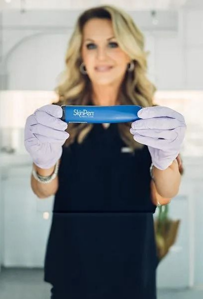 Woman in gloves holding a blue SkinPen device, smiling in a clinical setting.