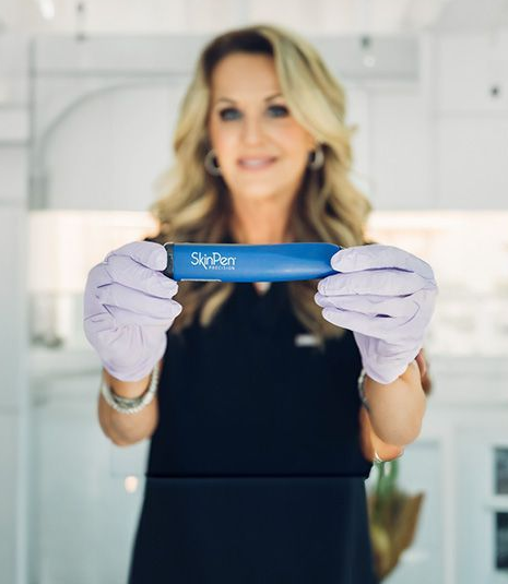 Woman in gloves holding a blue SkinPen device, smiling, in a bright setting.