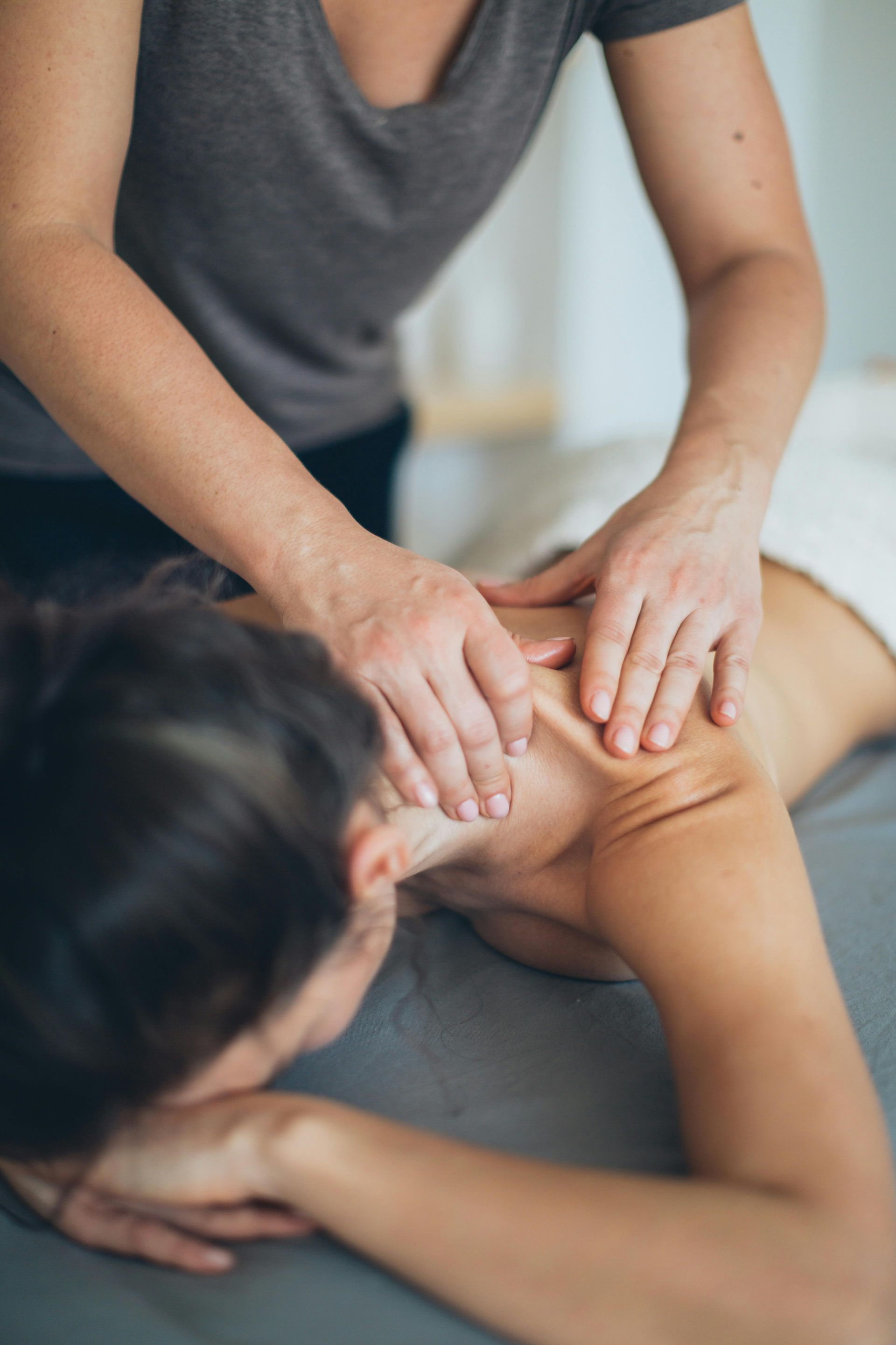 Person receiving massage on neck and shoulders; therapist's hands apply pressure.