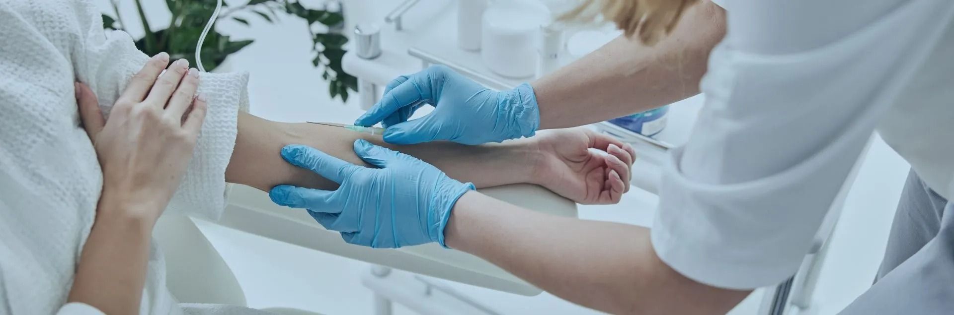 A person receiving an IV, with medical personnel wearing blue gloves preparing the arm.