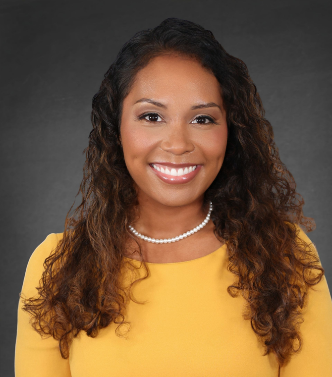 Smiling woman in a yellow top and pearl necklace against a dark gray background