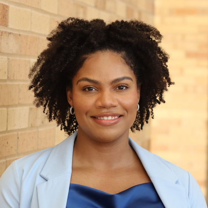 Smiling woman in a light blue blazer standing against a brick wall