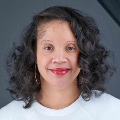 Portrait of a smiling person with curly dark hair against a gray background