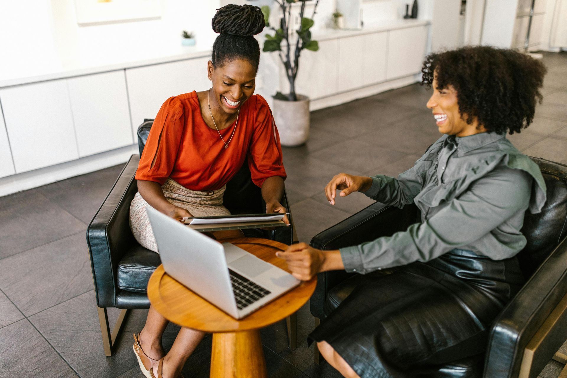 Two people seated with a laptop on a small table in a bright living room, smiling and talking