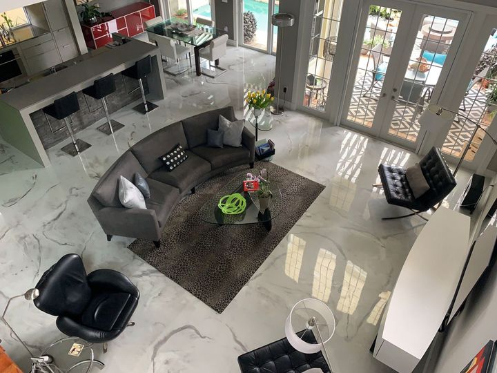 High-angle view of a modern living room with a curved gray sofa, a brown area rug, leather chairs, and an open kitchen.