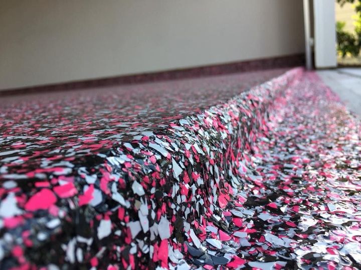 Close-up of a garage floor with a decorative epoxy finish featuring a speckled pattern in black, white, and bright pink.