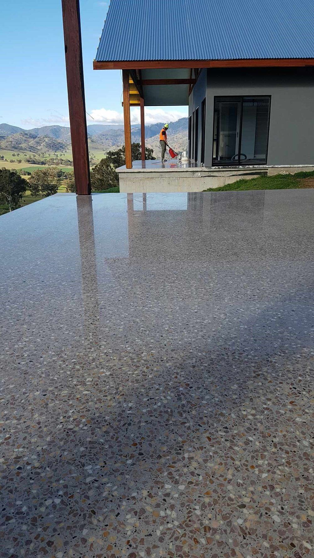 A polished concrete deck overlooks a scenic valley with a modern house and a person working on the porch.