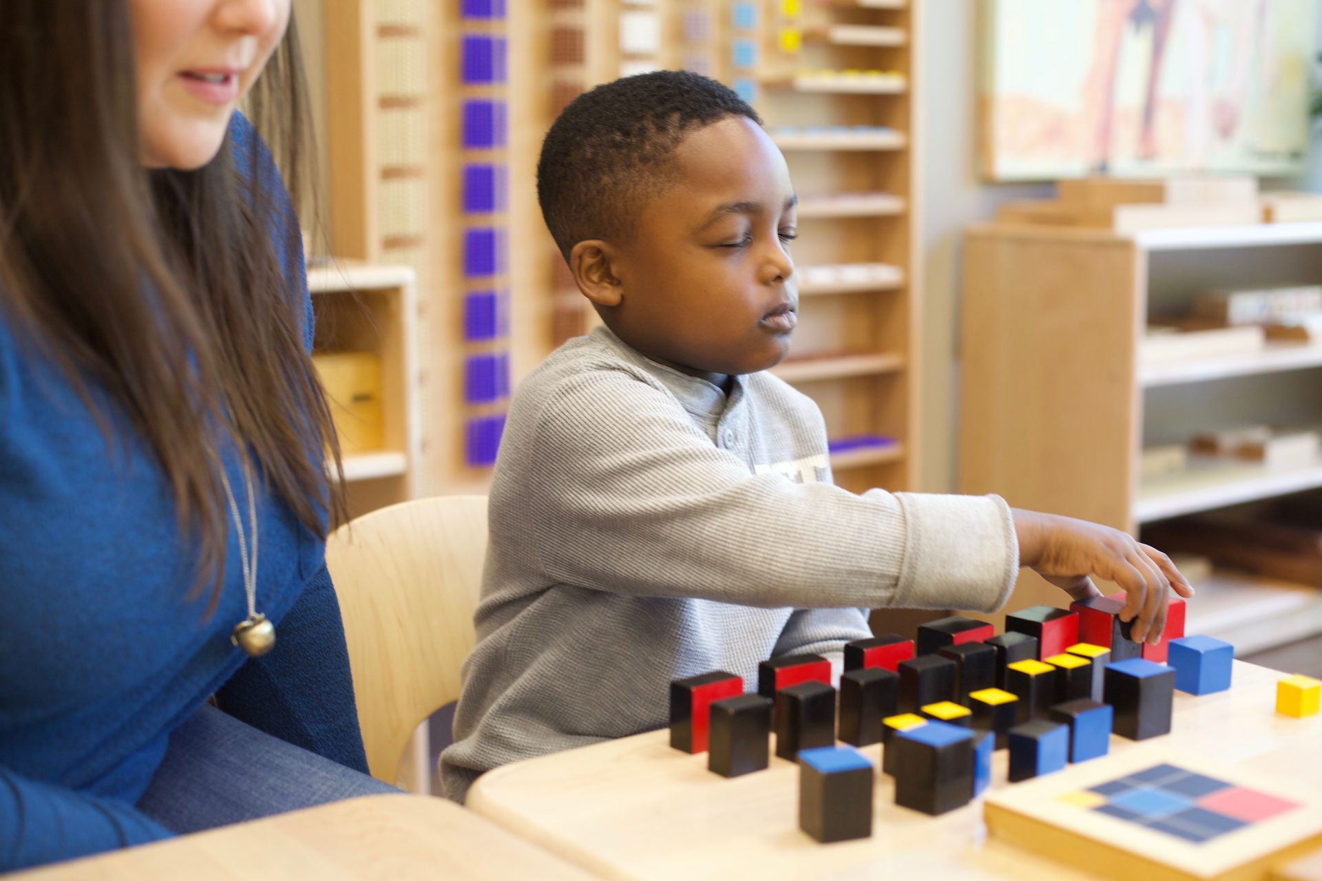 Child arranging trinomial cube at a table with an adult in a classroom setting