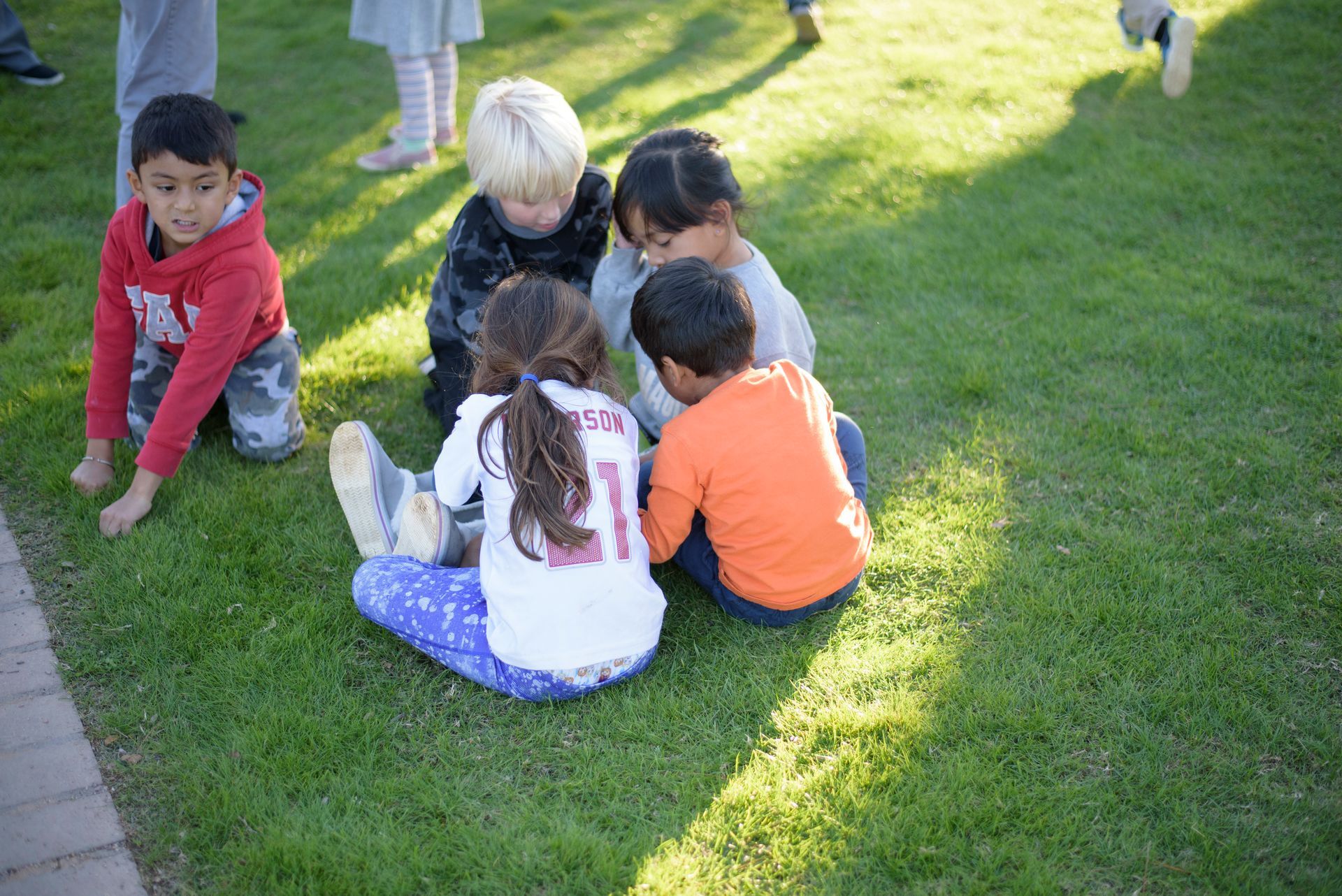 Children sitting and playing together on a grassy lawn in bright sunlight