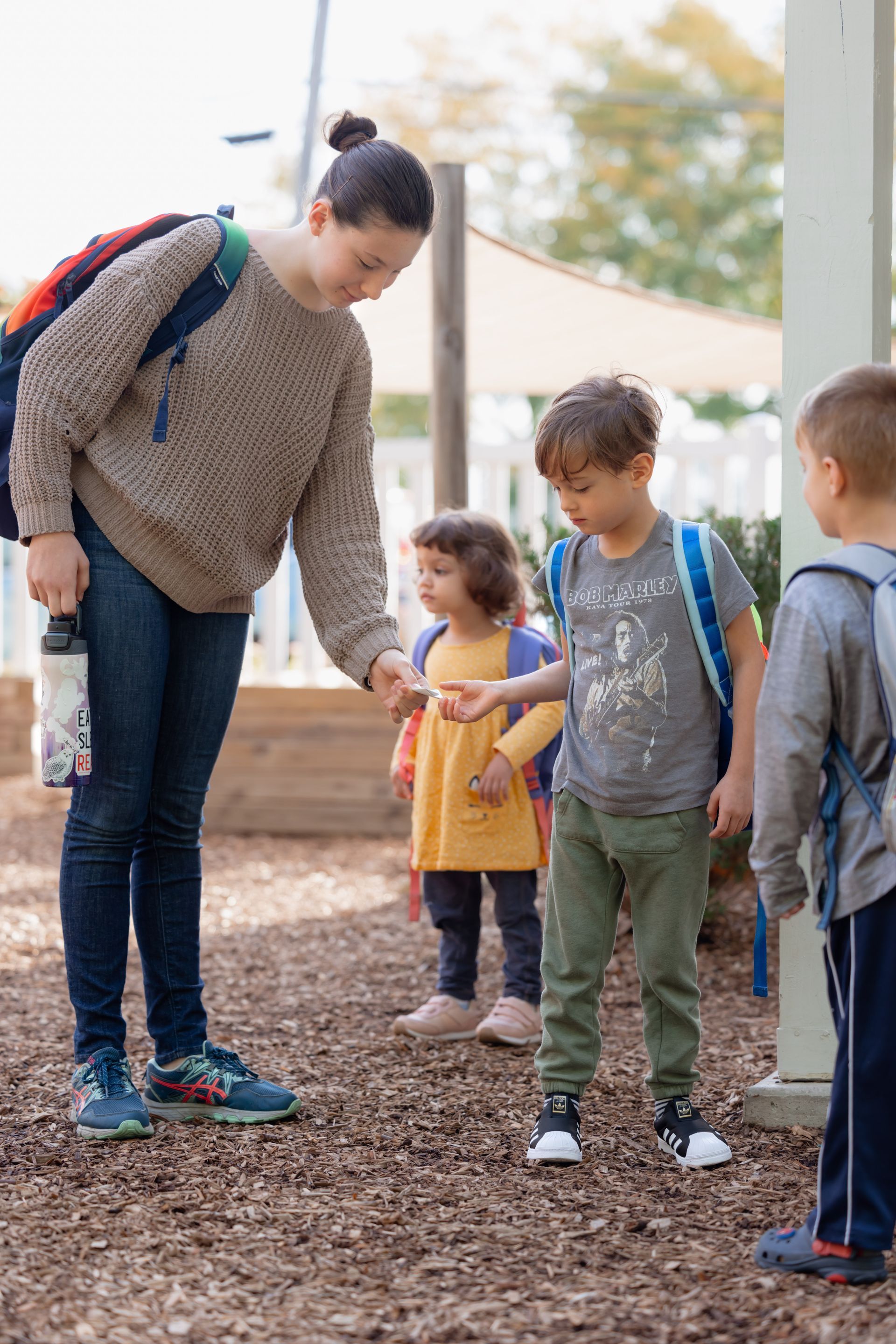 Teacher bending down to talk with three children standing outdoors on a playground path