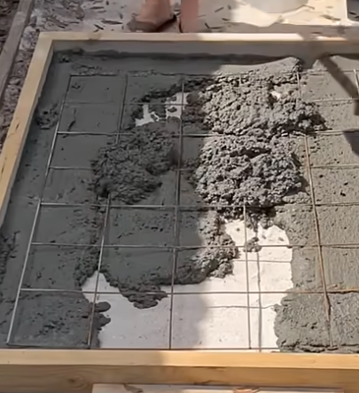 A person is pouring concrete into a wooden frame.
