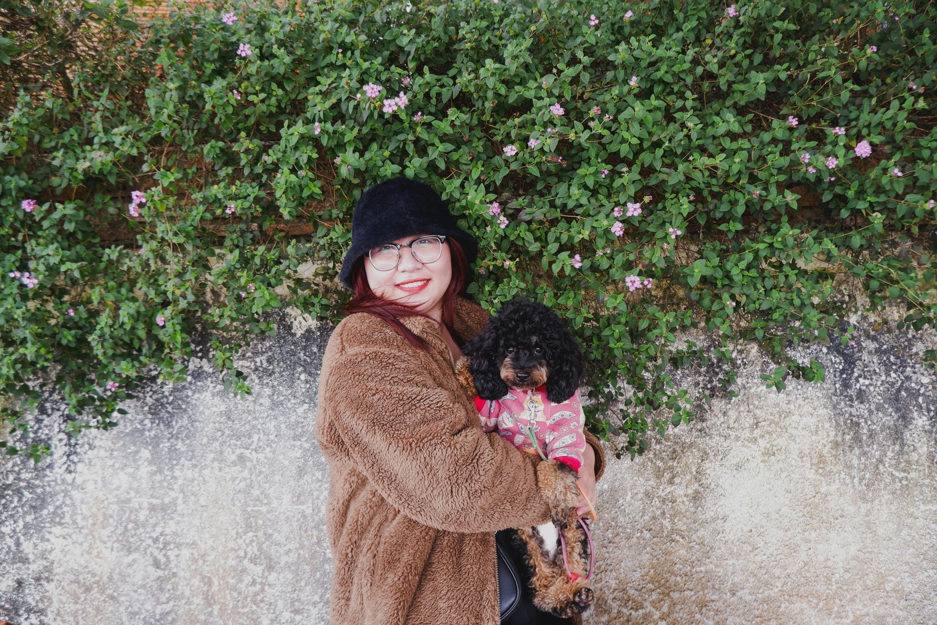 A woman is holding a small black dog in her arms.