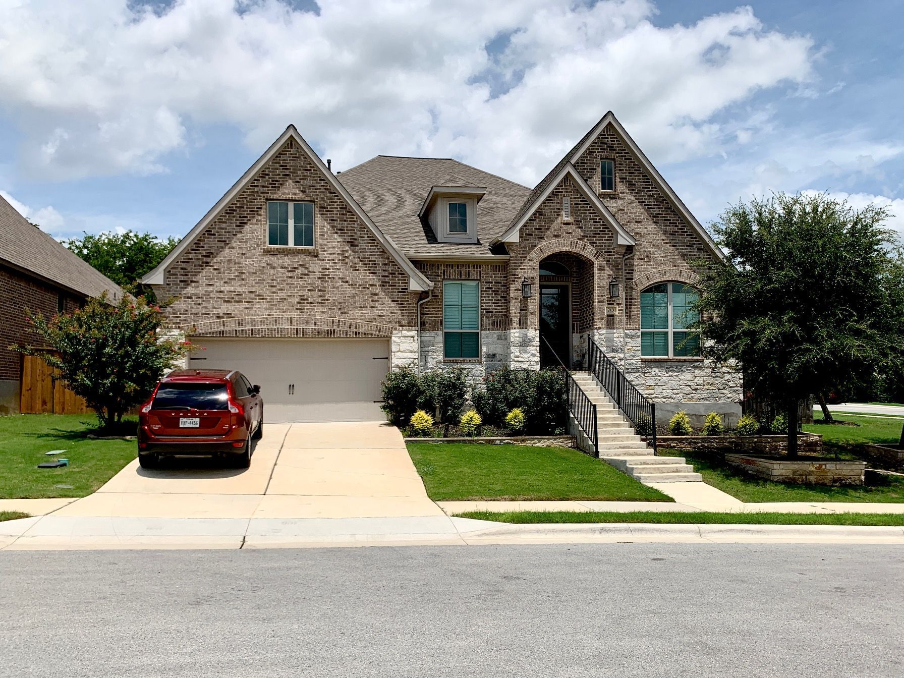 Suburban brick house with a red car parked in the driveway and a landscaped front yard