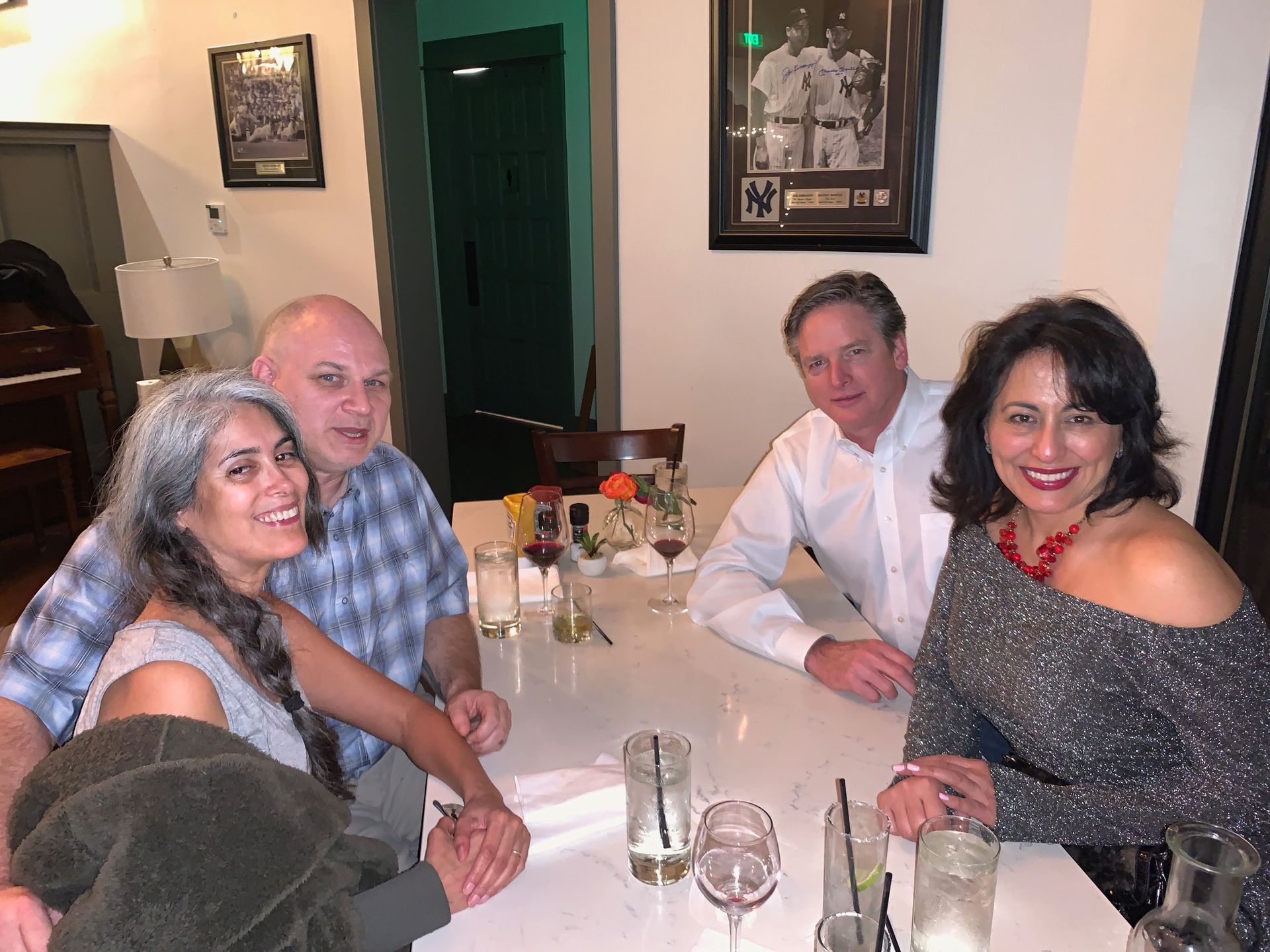 Four people seated at a restaurant table, smiling and talking with drinks and glasses nearby.