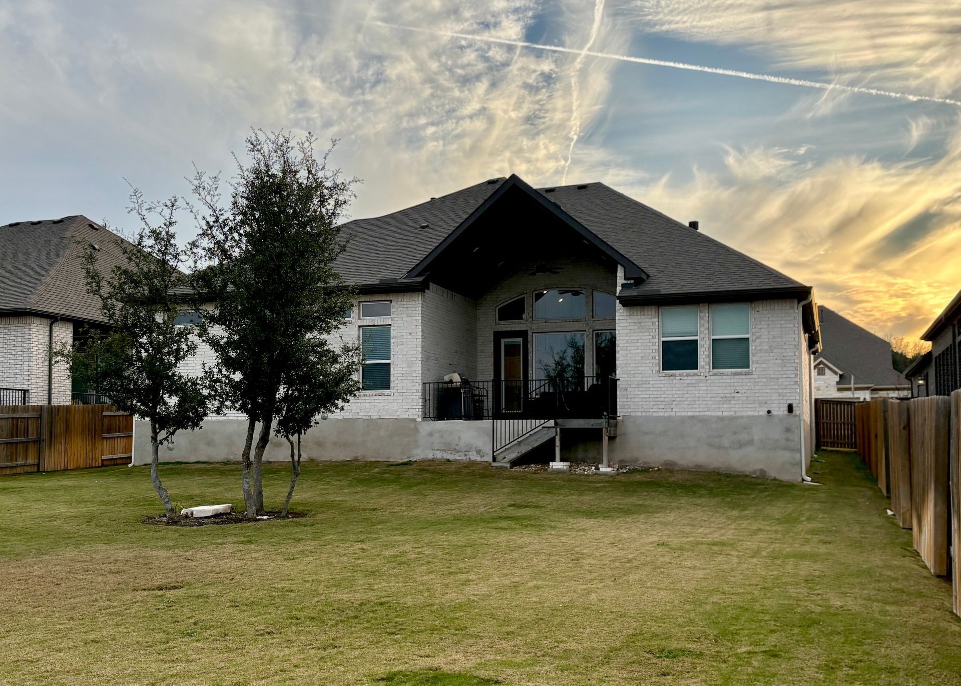 Small gray house with a front porch, fenced yard, and a sunset sky overhead