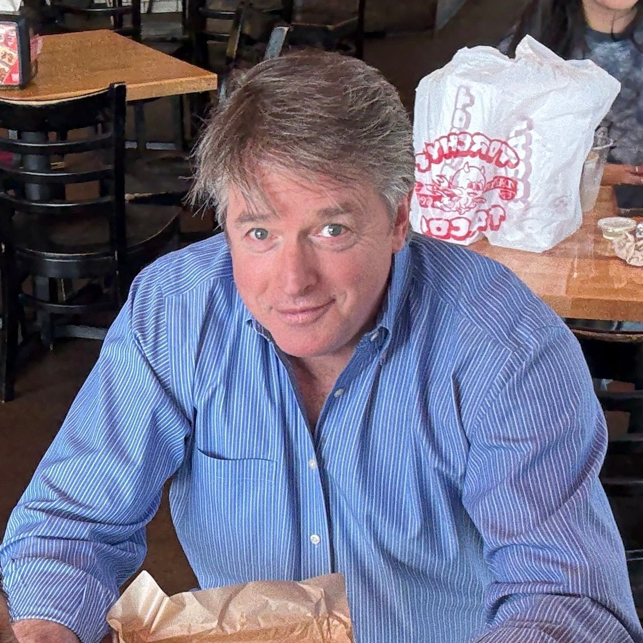 Man in a blue shirt seated at a restaurant table, looking at the camera.