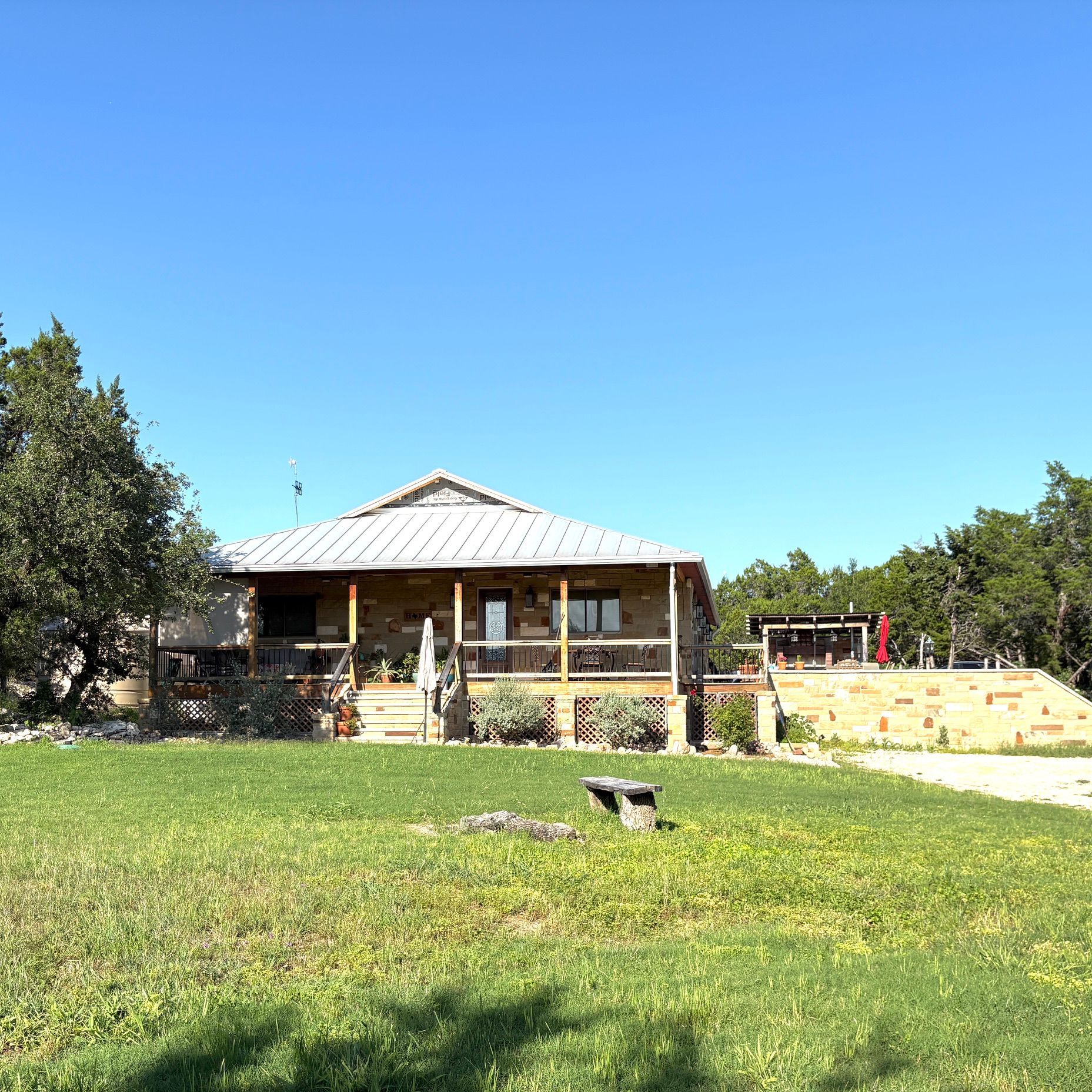 Stone house with a porch in a grassy yard under a bright blue sky