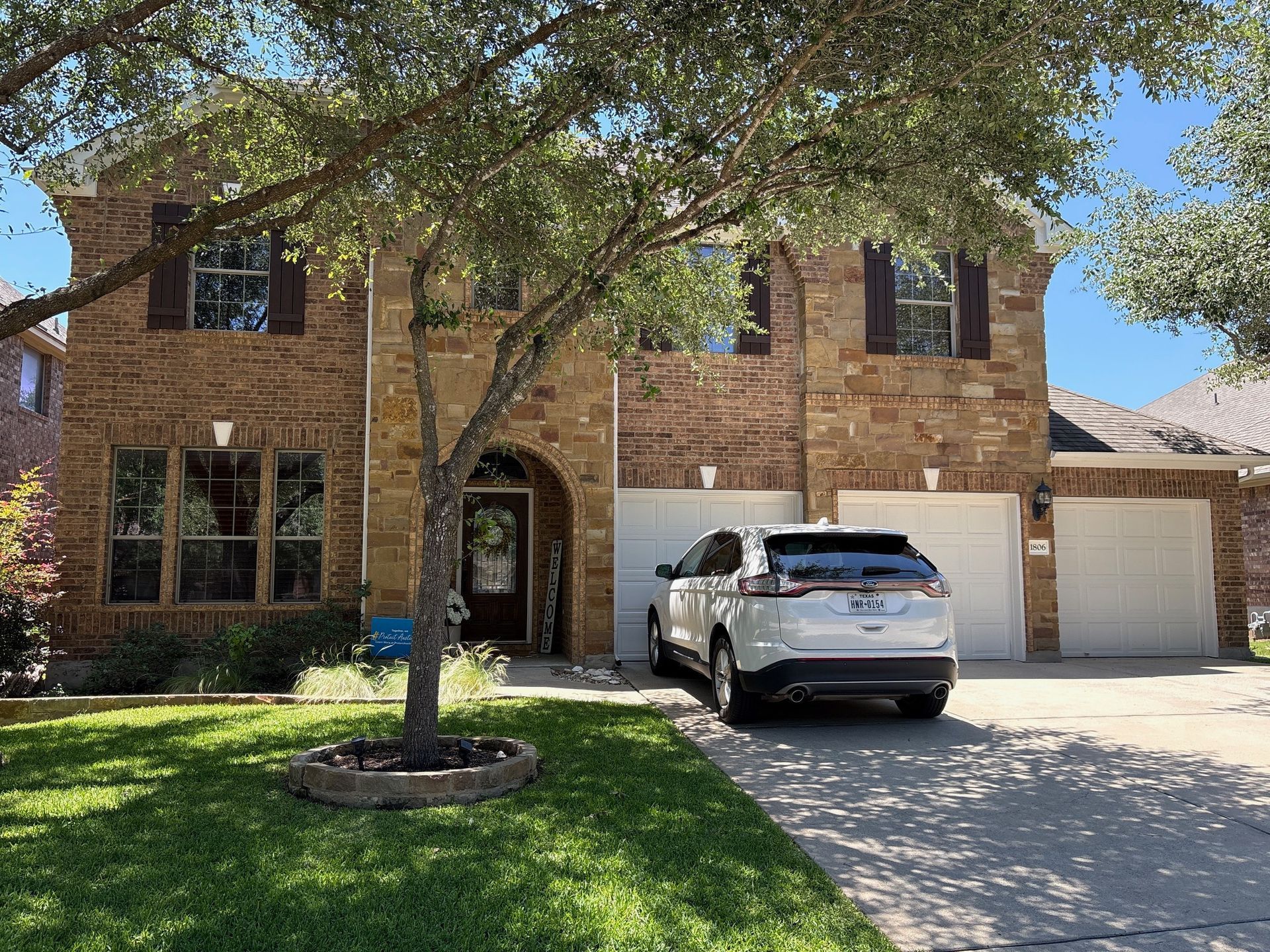 Brick two-story house with a tree-lined front yard and a white SUV in the driveway
