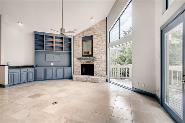 Spacious empty living room with stone fireplace, built-in cabinets, large windows, and tiled floor
