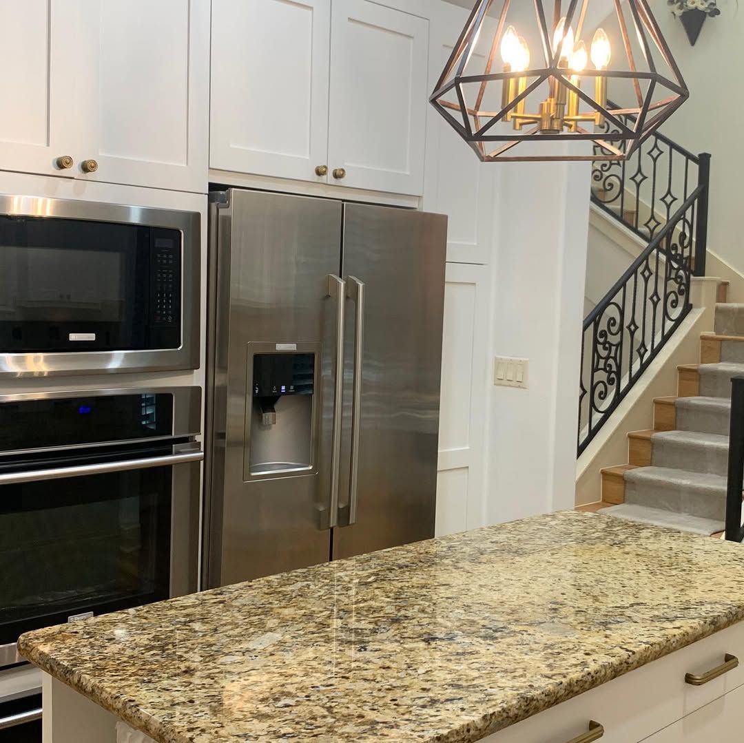 Modern kitchen with stainless steel appliances, granite island, and staircase in the background