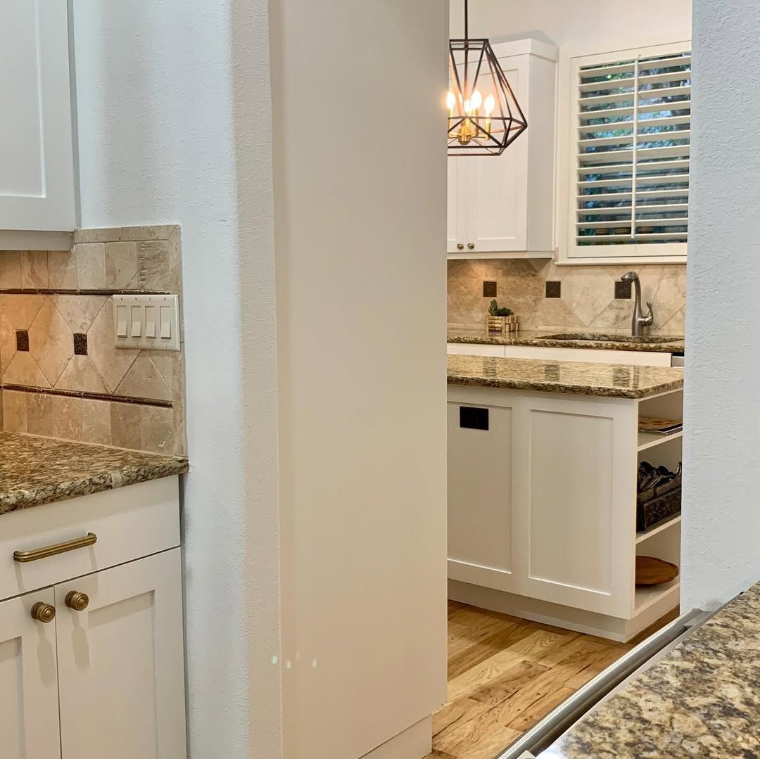 Bright white kitchen with granite countertops, tile backsplash, and pendant light viewed through a doorway