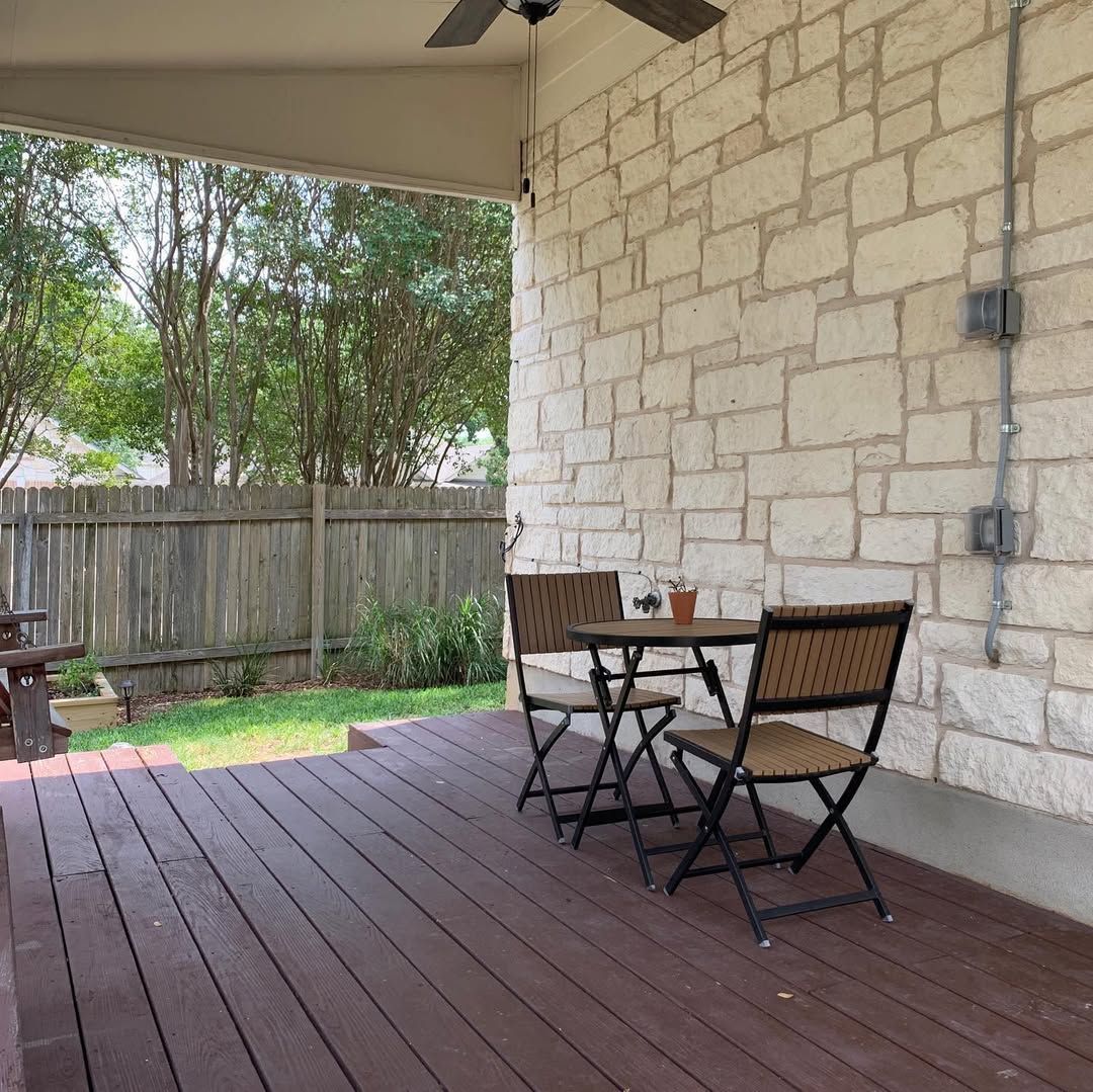 Covered patio with wooden deck, stone wall, and a small table with two chairs beside a fenced yard.