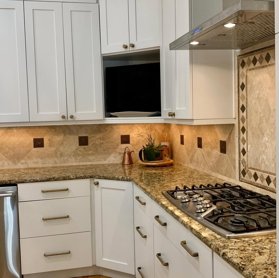 Modern white kitchen with granite countertops, gas cooktop, and beige tiled backsplash