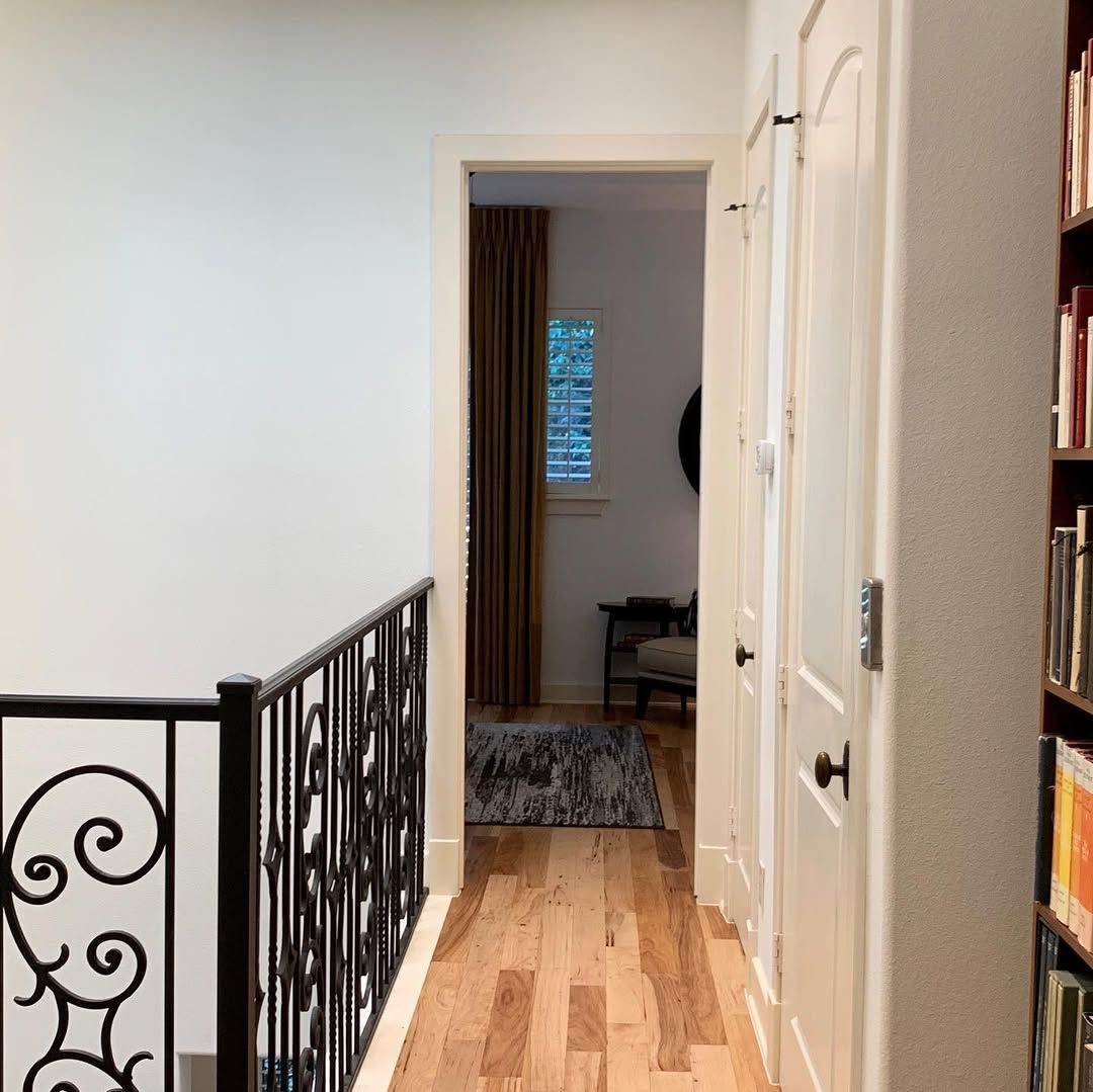 Hallway with hardwood floors, white walls, and an open doorway leading to a dim room.