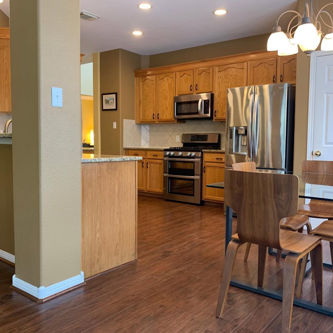 Warm kitchen with wood cabinets, stainless steel appliances, hardwood floor, and dining chairs in the foreground